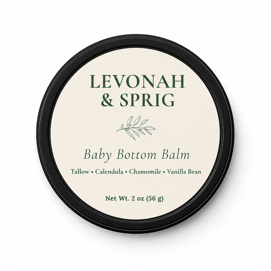 Levonah & Sprig Baby Bottom Balm in a 2 oz matte black tin with a cream botanical label, handcrafted tallow balm for delicate baby skin on a white background.