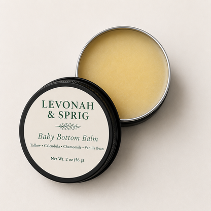 Open 2 oz tin of Levonah & Sprig Baby Bottom Balm showing creamy tallow balm beside the labeled matte black tin on a white background.